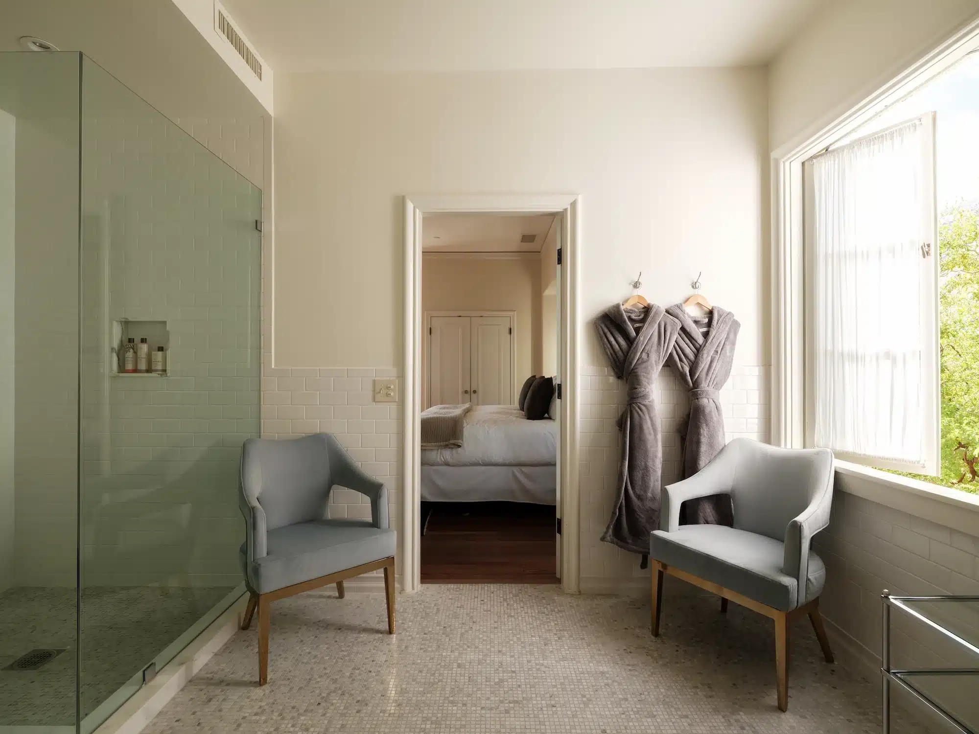 Rose bathroom with shower, chairs and doorway leading to bed